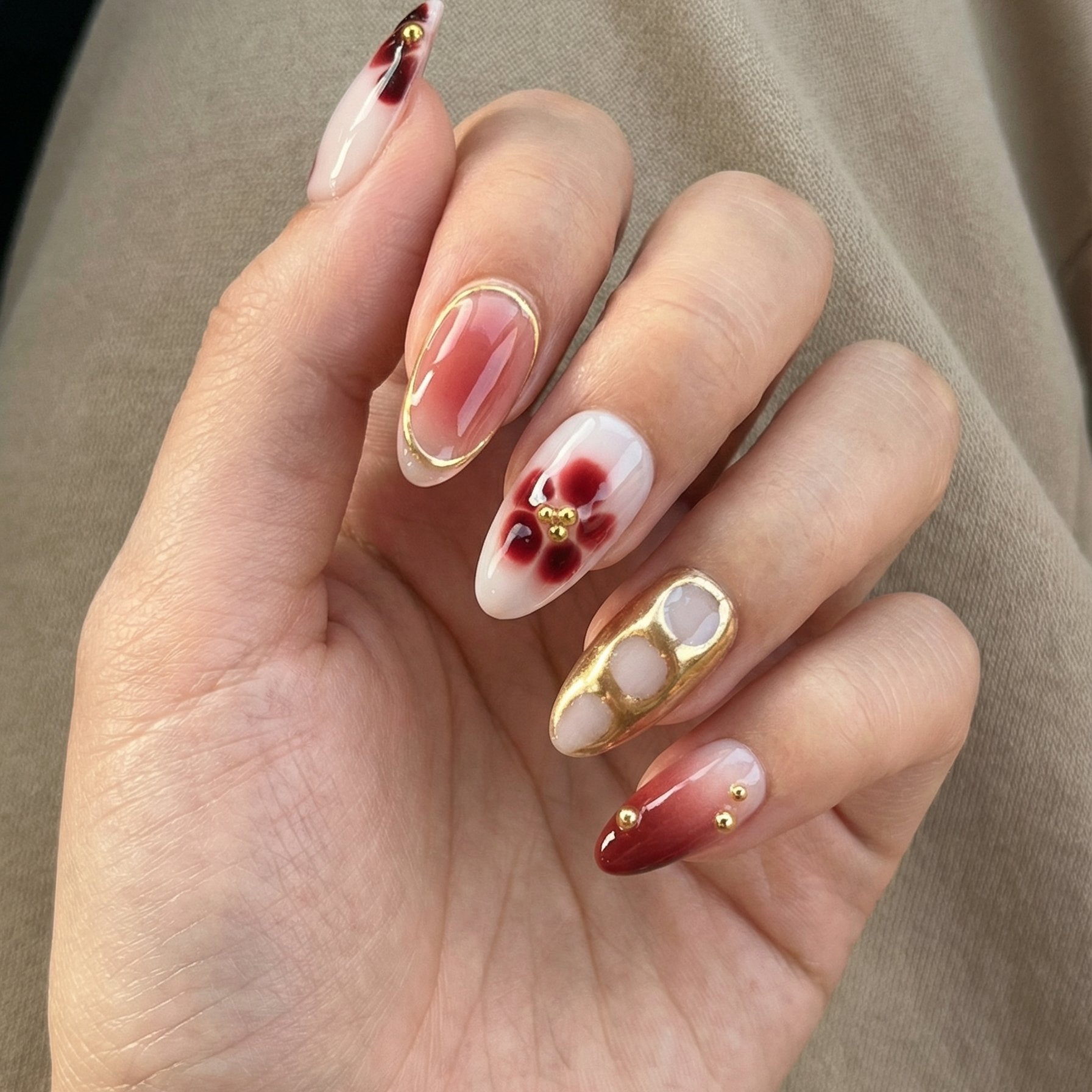 Hand with intricately designed nails featuring gold accents and red patterns.