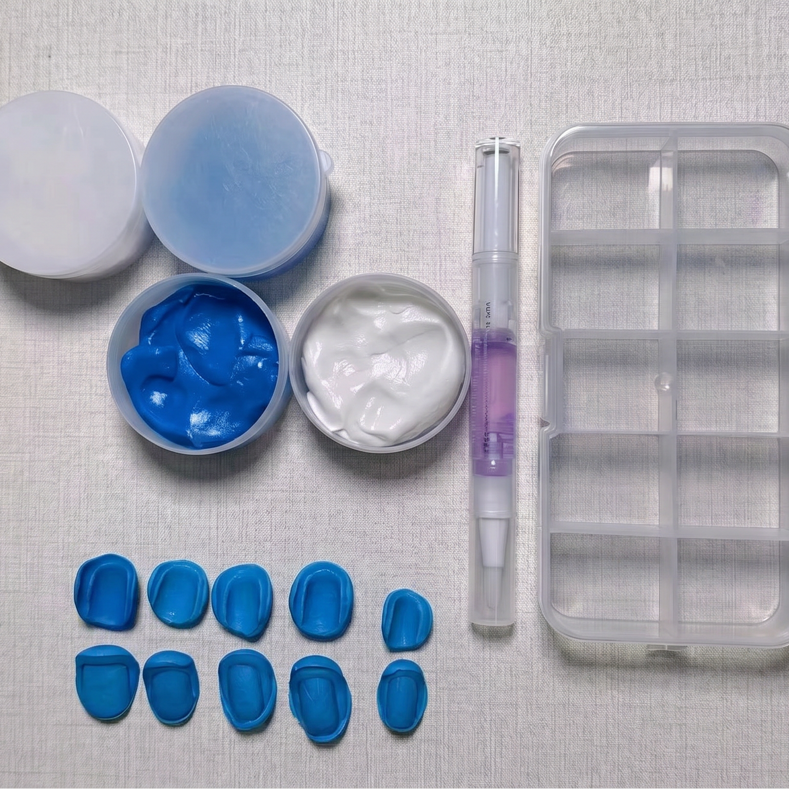 Collection of press on nails mold kit tools and materials including blue impression material, a tray, and other components on a textured surface.