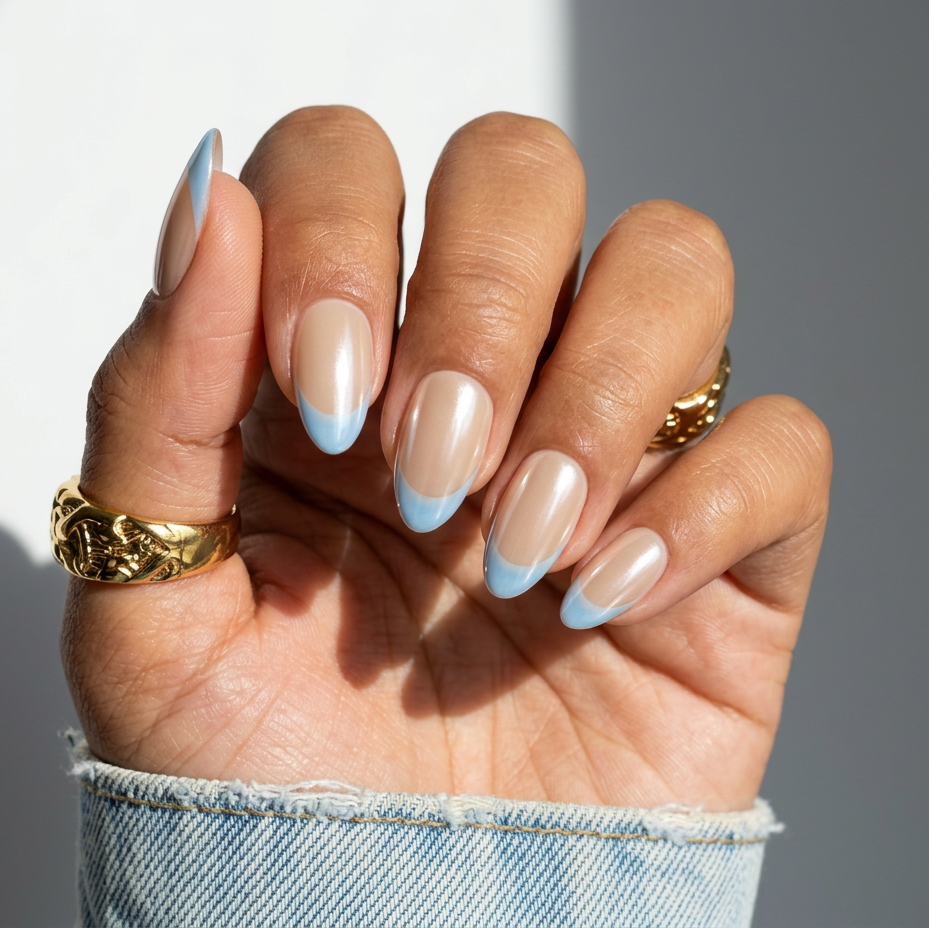 Hand with beige and blue nail polish wearing gold rings on a neutral background