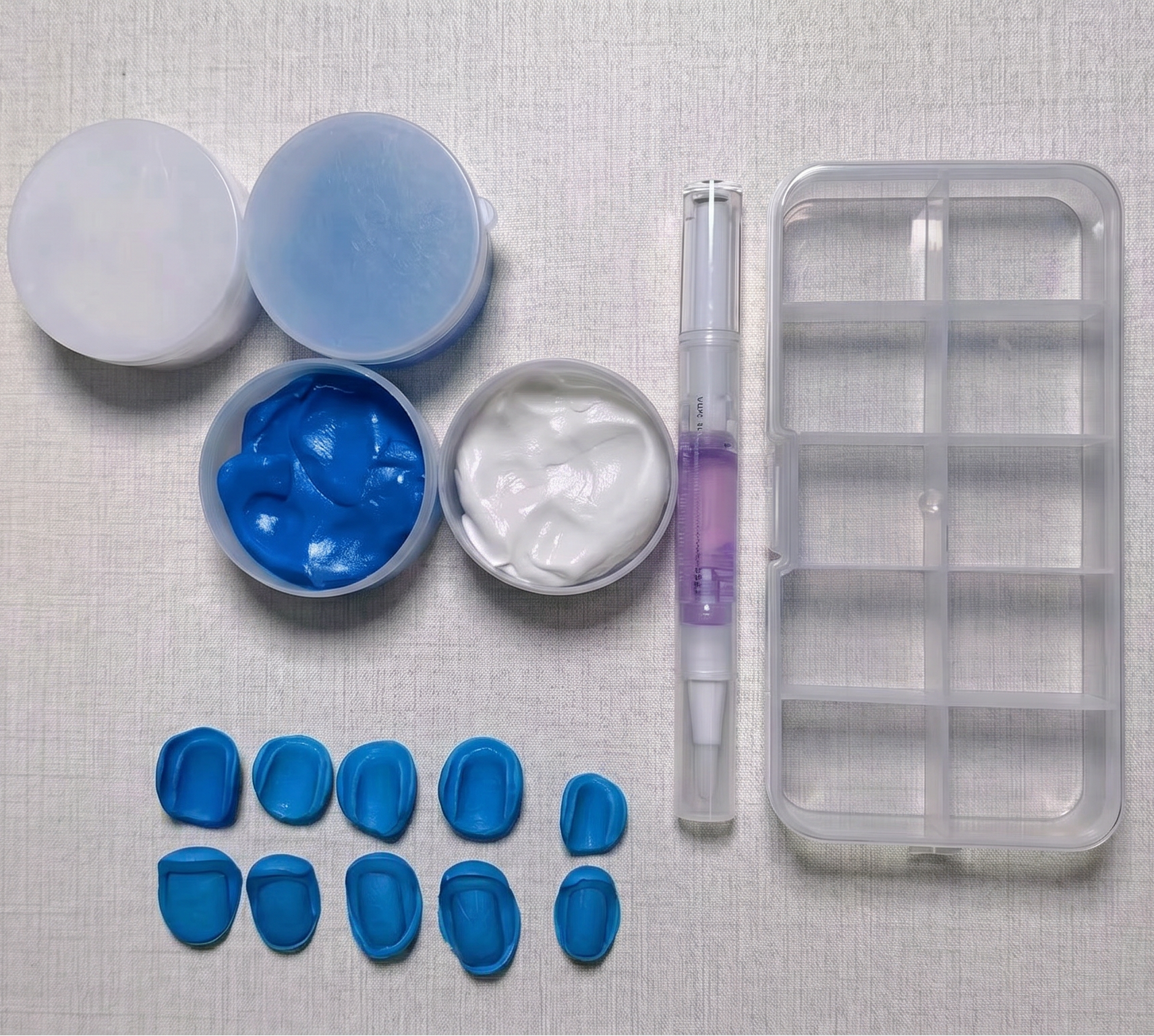 Collection of press on nails mold kit tools and materials including blue impression material, a tray, and other components on a textured surface.