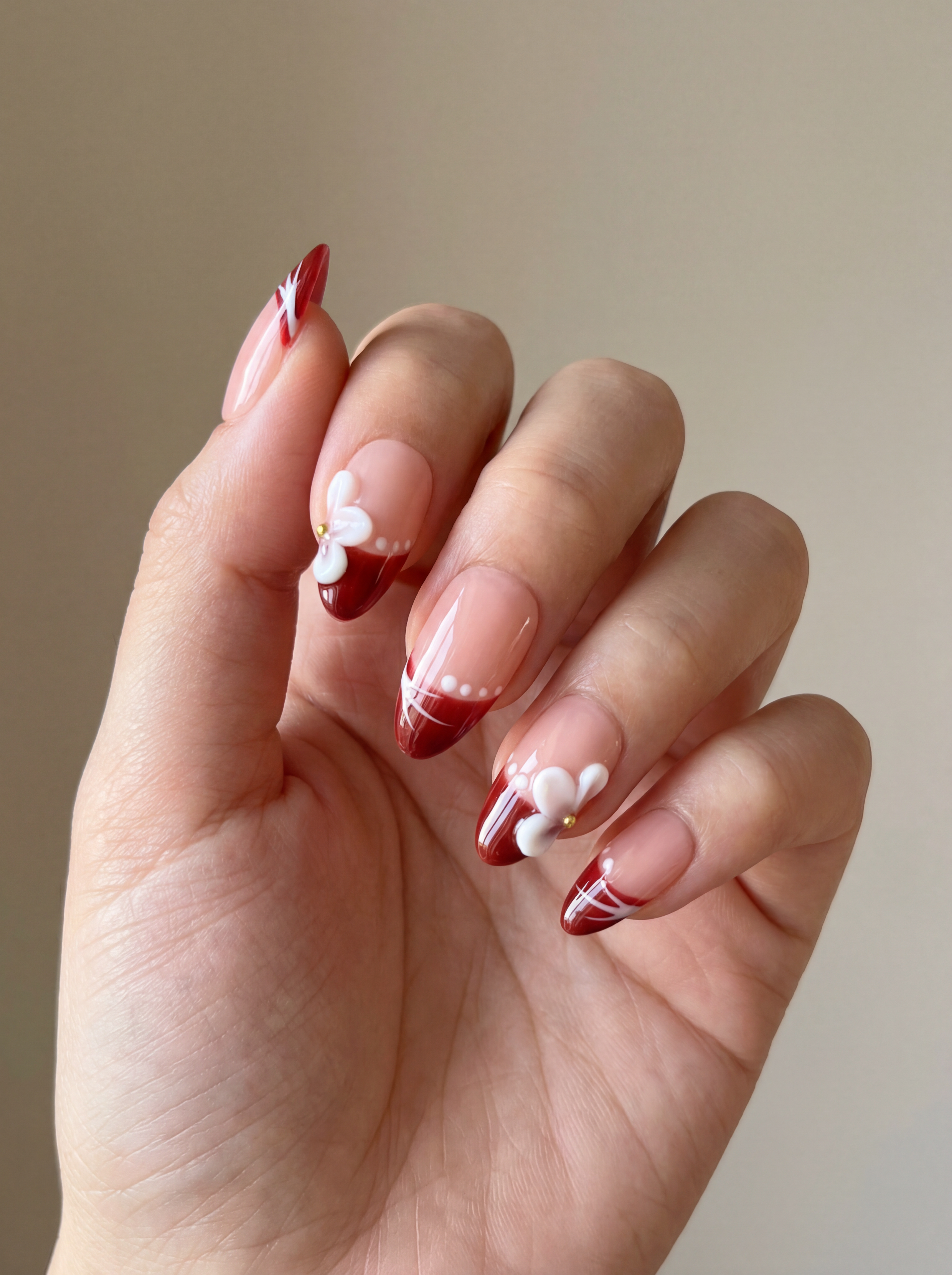 Hand with red and white nail design on a neutral background
