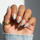 Hand with beige and blue nail polish wearing gold rings on a neutral background